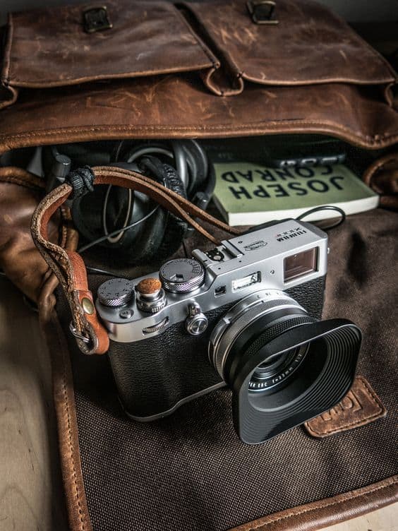 Vintage camera with leather strap and accessories in a travel bag, ideal for photography enthusiasts.